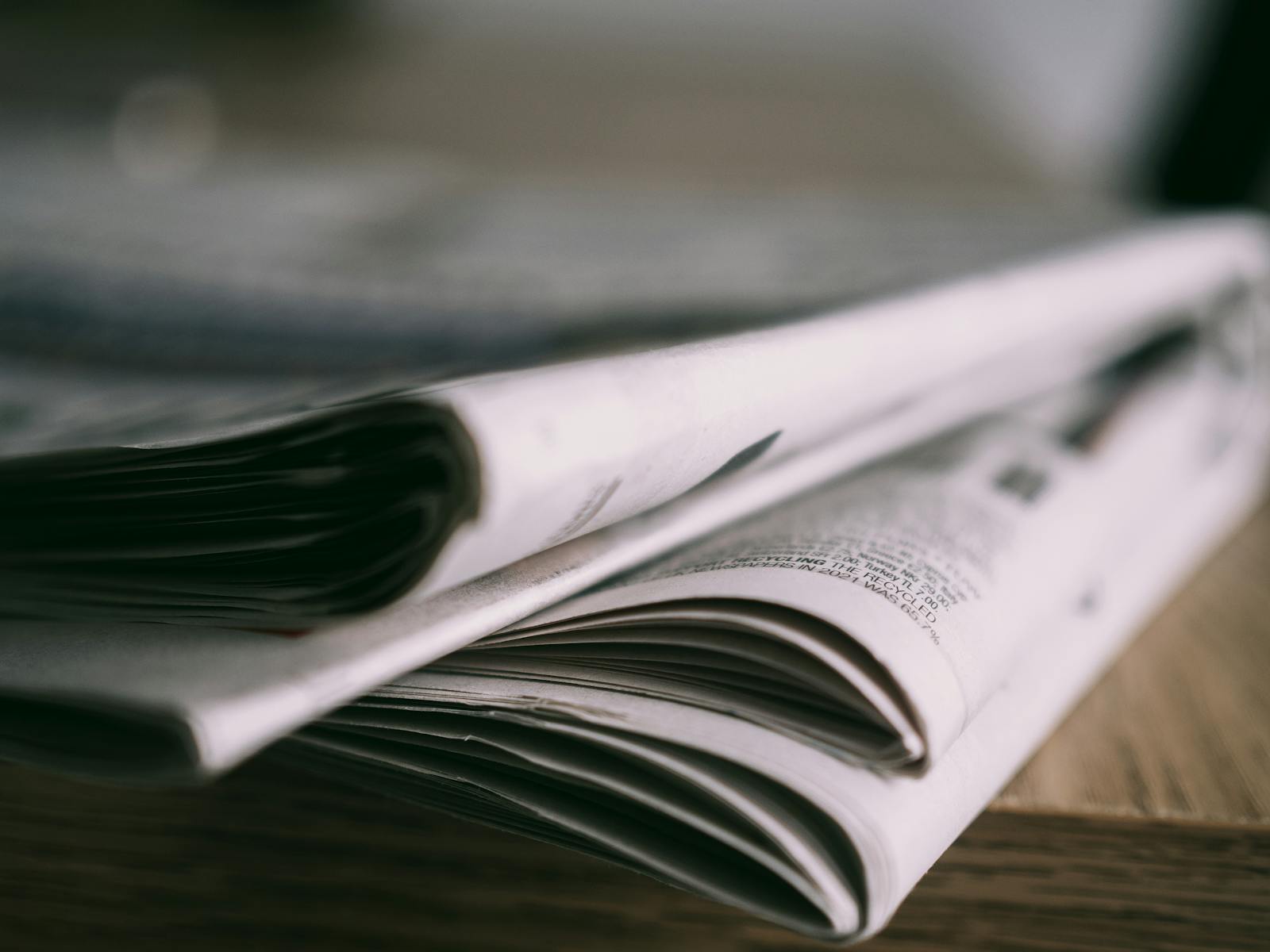 Stack of folded newspapers on a wooden table with a focus on printed pages.