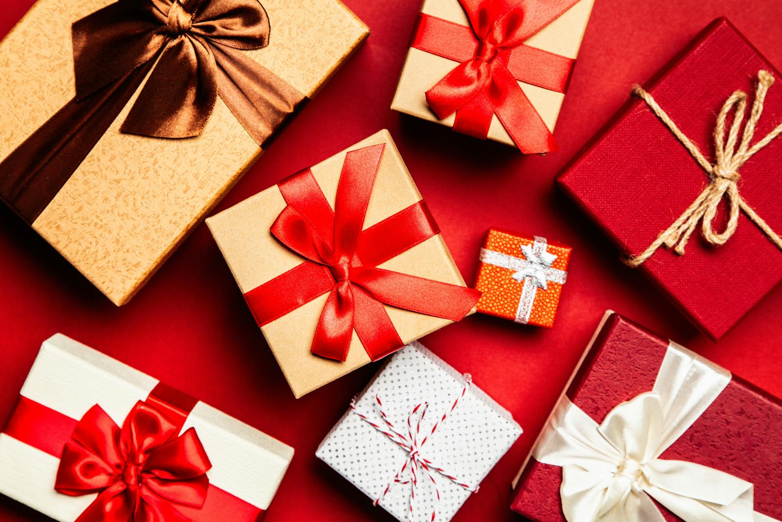 Top view of beautifully wrapped holiday gifts with red and brown ribbons on a vibrant red background.