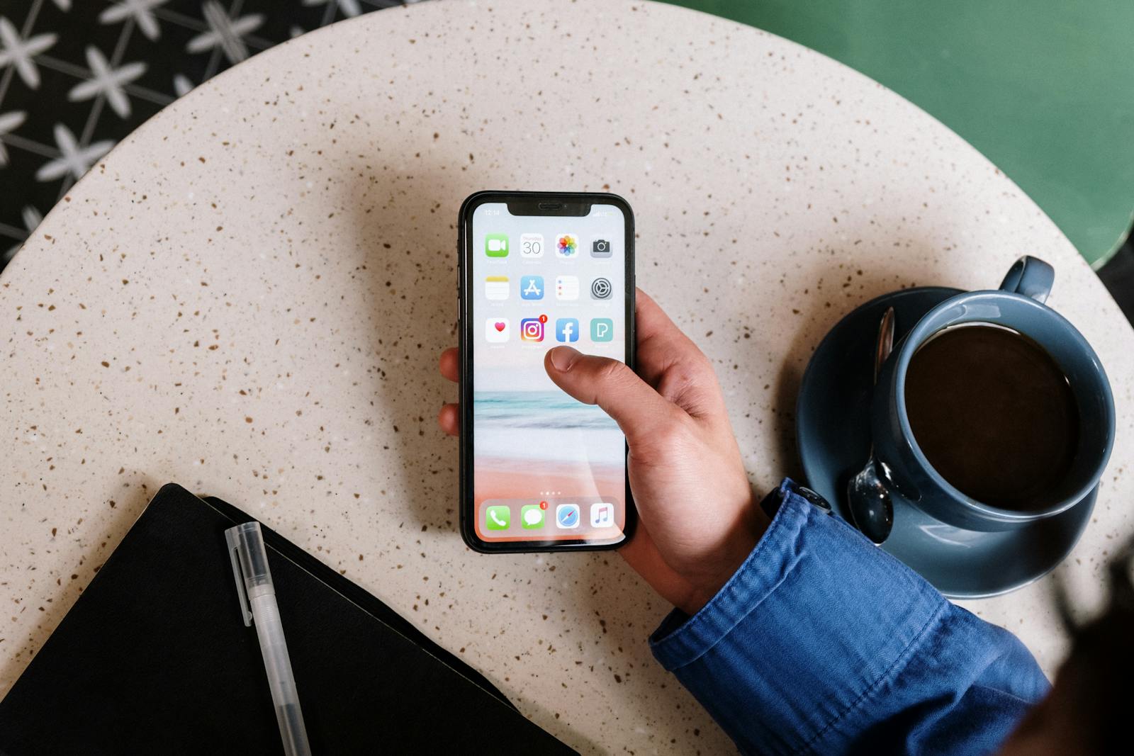 Person interacts with smartphone and coffee on a terrazzo table, showcasing apps and casual lifestyle.