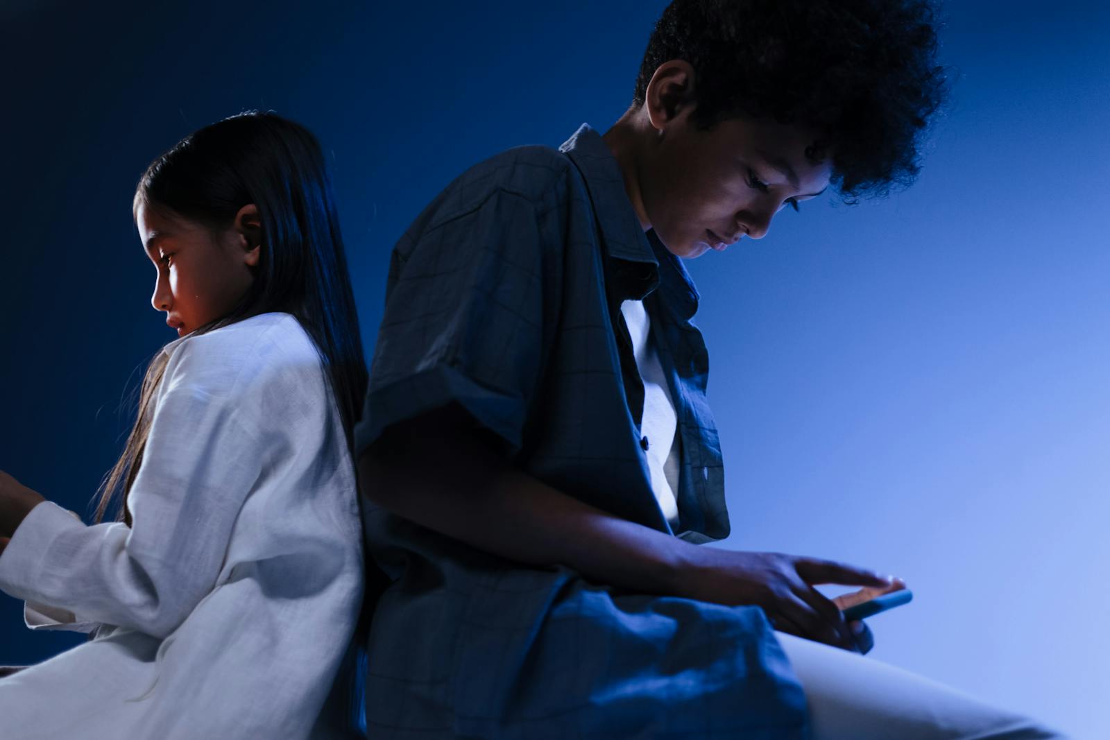 Young boy and girl using mobile devices in a conceptual studio setting with blue lighting.