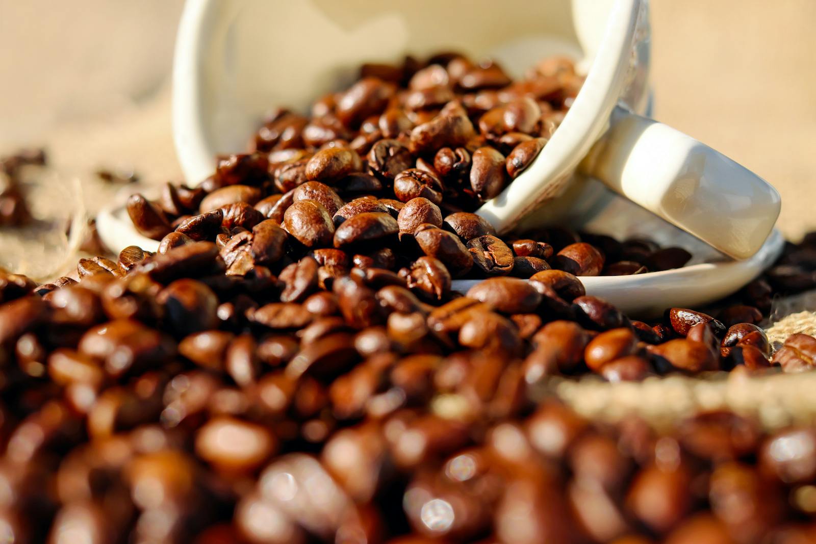 Close-up of coffee beans spilling from a cup onto a burlap surface, perfect for coffee lovers.