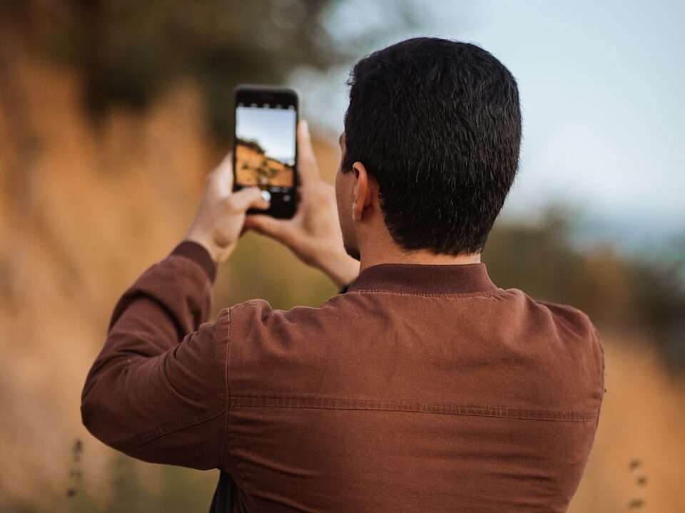 man in brown long sleeve shirt taking photo of sunset